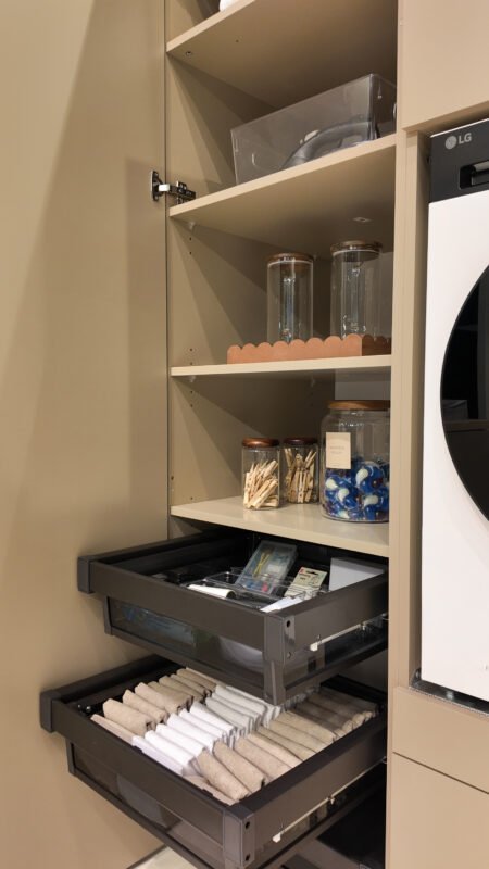 Hoge wasmachinekast met open planken en uitschuifbare lades gevuld met wasessentials en accessoires