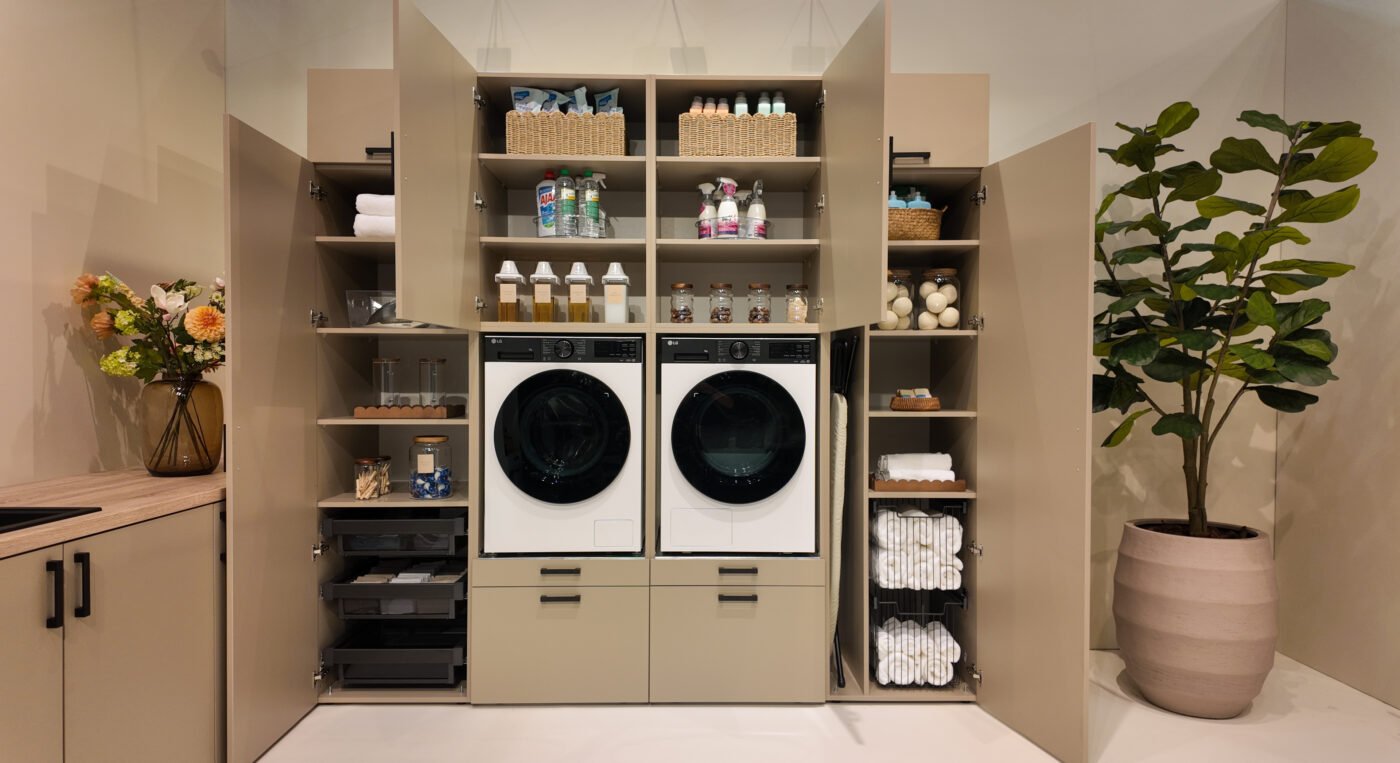 Wasmachinekast met open deuren gevuld met wasmiddelen, handdoeken en accessoires naast wasmachine en droger
