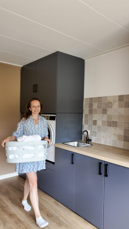 Bertie met een wasmand voor de wasmachinekast op hoogte
